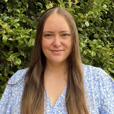 Candidate Annalise Mercer smiling in front of a green leafy background. Annalise has long brown hair and a blue floral top