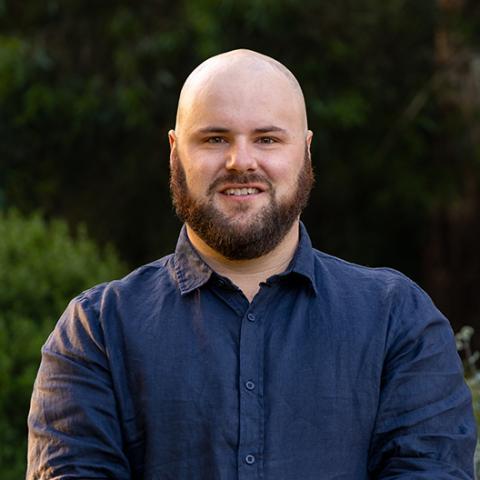 Proflie picture of Sam McColl, Greens candidate for Eureka. Sam is standing in front of blurred out parklands and is wearing a navy blue shirt