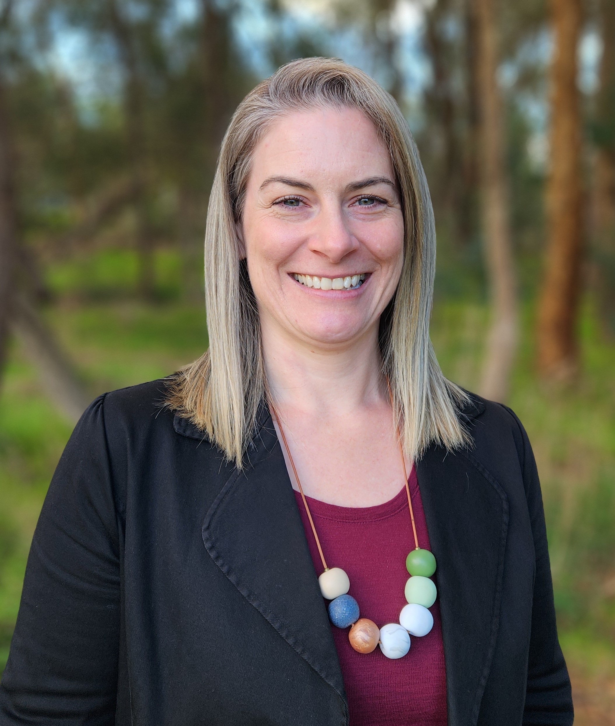 Merran in black blazer, purple top and necklace smiling