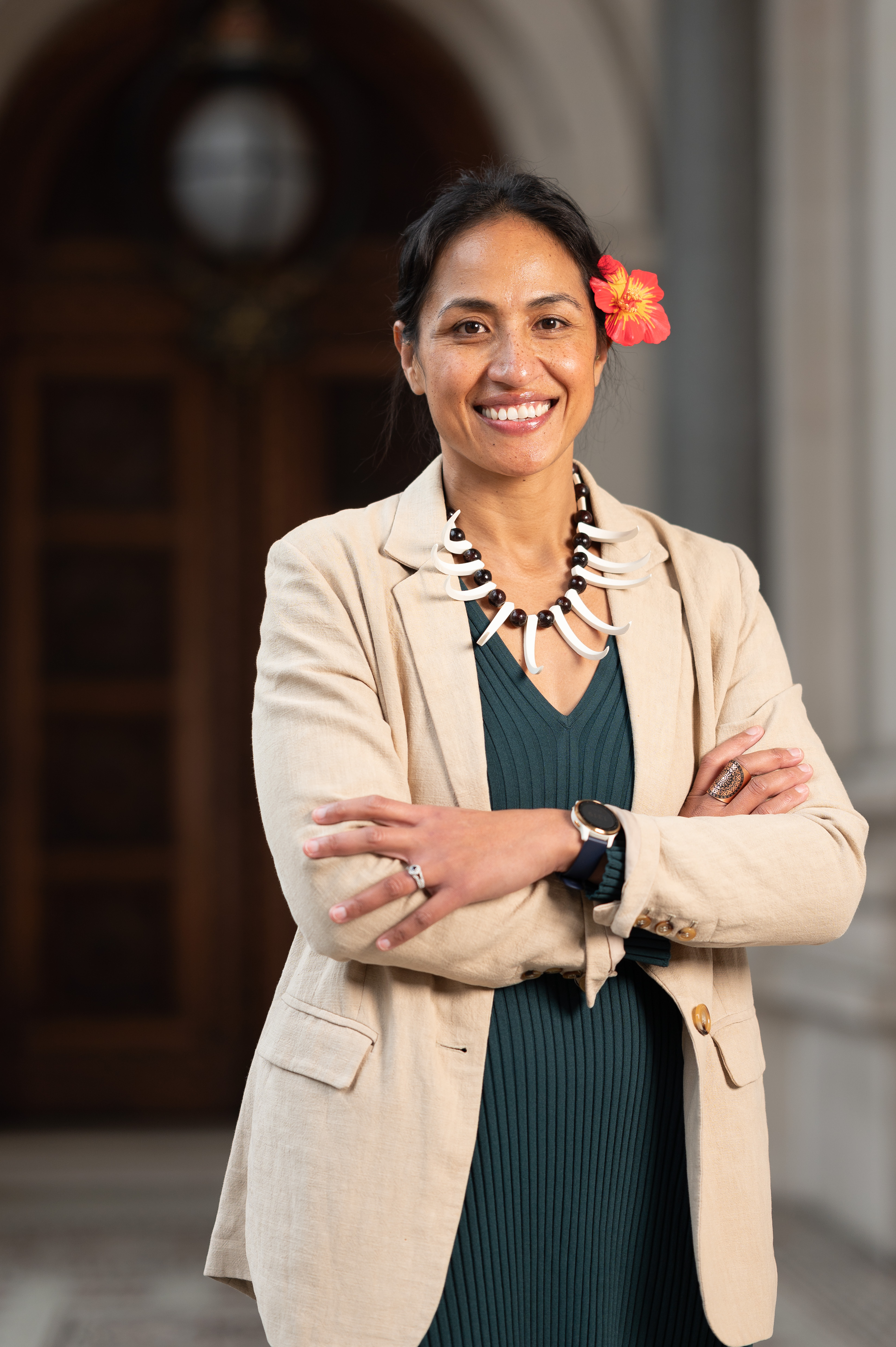 Anasina in a cream blazer, orange flower in her hair, arms crossed and smiling