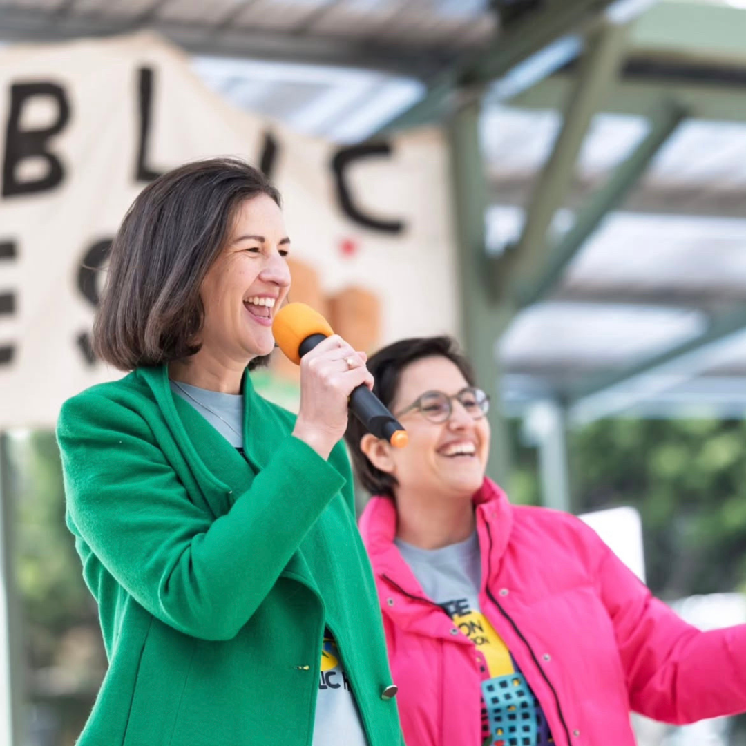 Image of Ellen Sandell smiling and speaking in micorphone wearing a green jacket