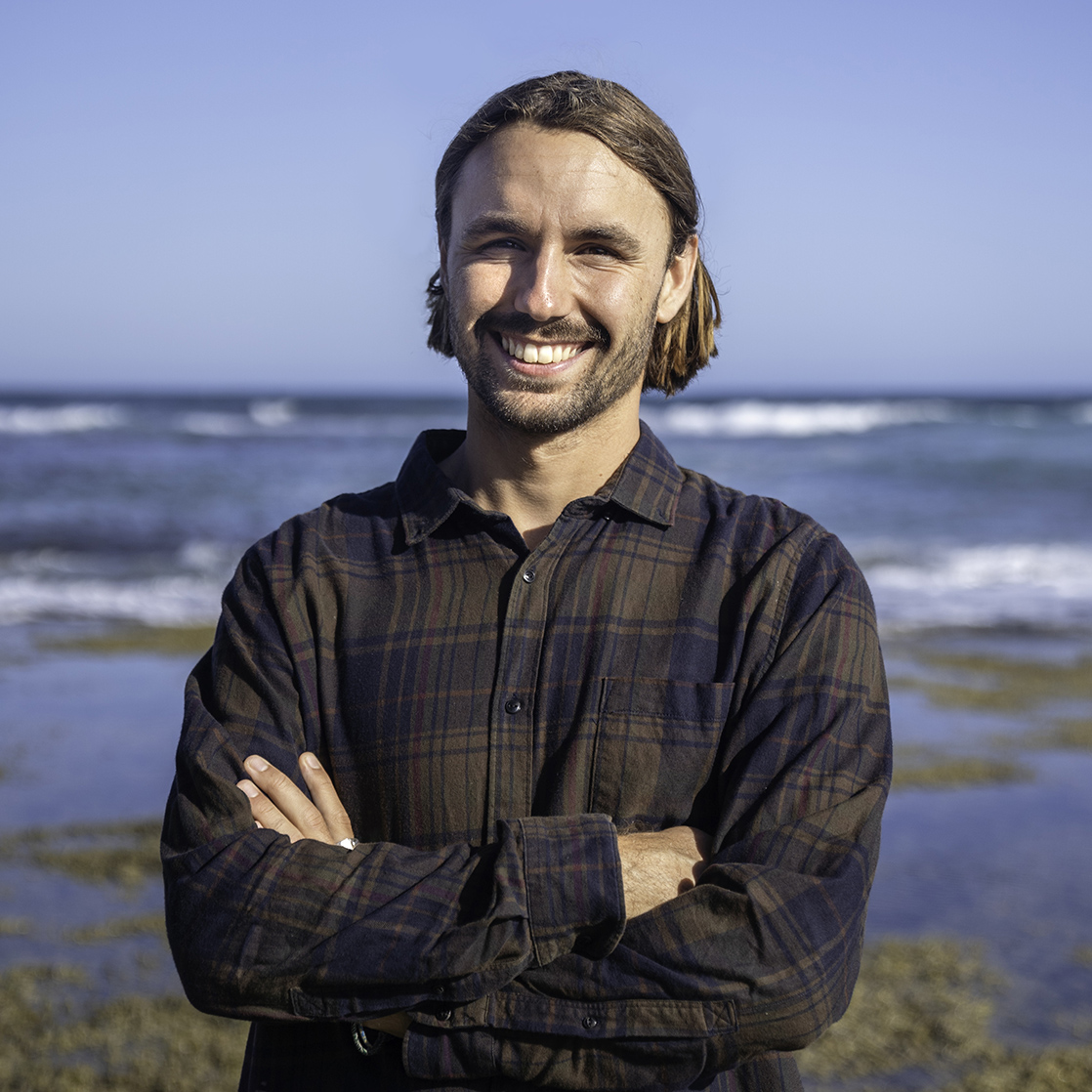 Candidate photo of Mitch Pope. Mitch is standing on a beach in front of sea