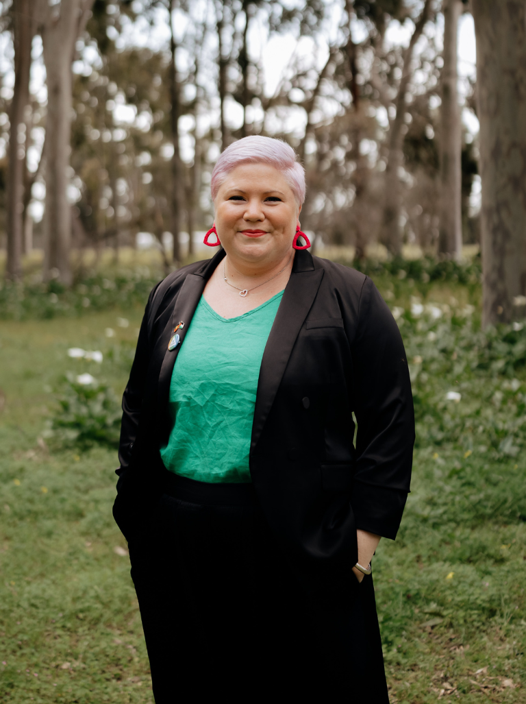 A woman is wearing a black blazer and green shirt and is smiling at the camera.