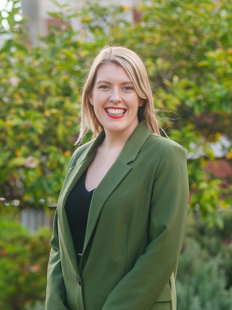 A woman is smiling at the camera and wearing a green blazer.