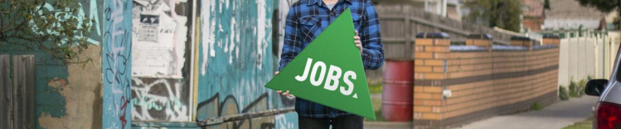 Image shows a person holding a green triangle sign with Jobs in white.