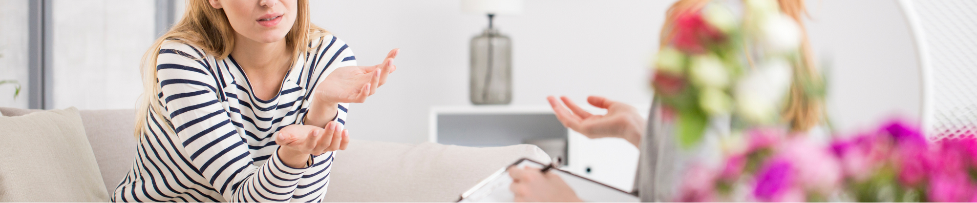 Image shows a patient sitting in front of a mental health practitioner, who is holding a notebook. No faces are shown.